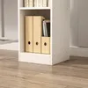 A close-up view of the bottom section of a white bookshelf, showing wooden magazine holders and books. Podgląd zdjęcia produktu