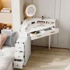 A white corner vanity desk with a lighted mirror and multiple drawers, set up in a room with a bed and shelving. Podgląd zdjęcia produktu