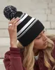 A woman wearing a striped beanie and a maroon jacket. Náhled obrázku produktu