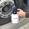 A person is using a white spray bottle with a black and blue pump mechanism to spray a truck wheel hub. Produktbild-Vorschau