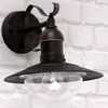A dark metal outdoor wall light with a clear glass globe is mounted on a white brick wall. Anteprima dell’immagine prodotto