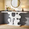 A white console table with a decorative base is placed against a wall with gray paneling. A bouquet of flowers in a blue vase, a stack of books with a decorative jar, and a table lamp are on top of the table. A scalloped gold mirror hangs on the wall above Anteprima dell’immagine prodotto