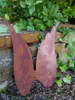 A rusty metal angel wing decoration is placed outdoors against a stone wall and greenery. Produktbild-Vorschau