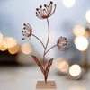 A decorative metal flower silhouette sculpture on a wooden base, set against a blurred background of bokeh lights. Produktbild-Vorschau