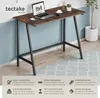 A desk with a laptop, phone, and cup on it, set against a blue and white wall with a rug on the floor. Produktbild-Vorschau