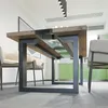 A dining table with a unique design, featuring a wooden top and a metal frame with a glass insert. Chairs are visible on either side, and a green kitchen cabinet is in the background. Produktbild-Vorschau