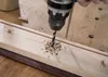 A close-up shot of a drill bit drilling into a wooden plank, creating wood shavings. Voir les images du produit