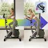 A woman is shown using a stationary bike in two different positions, with a graphic overlay illustrating the adjustable handlebars. The background features a window with a view of trees and a modern interior. Produktbild-Vorschau