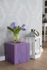 A purple wooden cube plant stand with a vase of purple hyacinths and a white lantern with a candle. Voir les images du produit