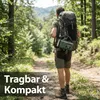 A person is hiking on a forest path, carrying a backpack with a radio attached. Produktbild-Vorschau