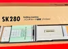 The image shows the inside of a cardboard box containing a knitting machine and its instruction manual. Produktbild-Vorschau