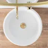 A top-down view of a white round sink with a gold drain and faucet, set against a wooden background. Náhled obrázku produktu