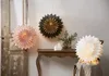 Three paper star lanterns are displayed in a room. One pink lantern hangs on a wooden door, a dark green and gold lantern hangs on the wall, and a white lantern sits on a chair. Podgląd zdjęcia produktu
