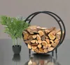 A round metal firewood rack filled with logs, placed next to a potted plant. Náhľad obrázku produktu