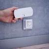 A hand is holding a white LED night light with a motion sensor above a wall socket with a plug-in adapter. Produktbild-Vorschau