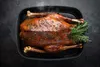 A roasted duck in a black roasting pan with herbs. Produktbild-Vorschau