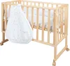 A wooden crib with a white sleeping bag hanging on the side. Produktbild-Vorschau