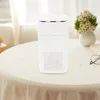 A white air purifier sits on a round table covered with a light-colored tablecloth. A vase with flowers and a pair of glasses are also on the table. Podgląd zdjęcia produktu