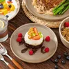 A close-up of a dessert on a plate, surrounded by other food items and cutlery, set on a wooden table. Náhled obrázku produktu
