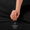 A hand is shown touching a black fabric, likely a bedsheet, with text overlay indicating the material composition. Produktbild-Vorschau