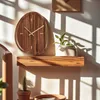 A wooden wall clock with gold hands is displayed on a shelf, casting shadows from sunlight. Voir les images du produit
