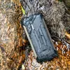 A rugged smartphone is partially submerged in water, resting on wet rocks and dry vegetation. Podgląd zdjęcia produktu