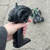 A hand holding a remote control for a toy car, with the car in the background. Náhľad obrázku produktu