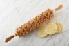 A wooden rolling pin with a chicken pattern and three cookies on a marble surface. Voir les images du produit