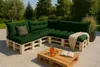 An outdoor patio setting with a sectional sofa made of pallets and green cushions, a coffee table with drinks and a book. Anteprima dell’immagine prodotto