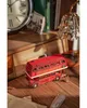 A vintage-style red double-decker London tour bus model sits on a wooden desk next to a clock and books. Náhľad obrázku produktu