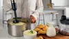 A person is using an immersion blender to make mashed potatoes in a pot, with potatoes, milk, and a bowl of mashed potatoes on the counter. Anteprima dell’immagine prodotto