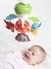 A baby lying on a white surface looking up at a mobile. Voir les images du produit