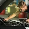 A mechanic is working on a car engine with a work light illuminating the area. Voir les images du produit