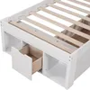 A close-up view of the lower section of a white bed frame, showing wooden slats and an open drawer with a wooden interior. Podgląd zdjęcia produktu