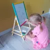 A young girl in a pink dress is sitting on the floor and drawing on a double-sided whiteboard easel. Náhľad obrázku produktu