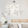 A white leaf-shaped pendant lamp hangs above a bed with wooden headboard and pillows. Produktbild-Vorschau