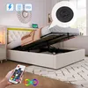 A bedroom scene with a bed that has its storage compartment open, showing the mattress and frame. A remote control is held in the foreground. Produktbild-Vorschau
