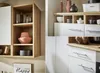 A collage of images showing different views of a modern kitchen unit with white cabinets and wooden accents, featuring decorative items and kitchenware. Produktbild-Vorschau