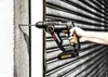 A hand holding a cordless hammer drill against a textured wall. Produktbild-Vorschau