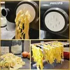 A collage showing a pasta maker and freshly made pasta. The top left shows pasta coming out of a pasta maker. The top right shows the side of a Philips pasta maker. The bottom left shows a pile of uncooked pasta and eggs. The bottom right shows pasta dryin Produktbild-Vorschau