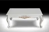 A white rectangular coffee table with ornate gold detailing on the legs and front apron, set against a gradient background from black to light gray. Náhľad obrázku produktu