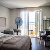 A bedroom with a bed, a fan, and a balcony overlooking the sea. Náhľad obrázku produktu