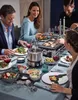 A group of people are enjoying a meal together around a table, with a fondue set and various dishes laid out. Voir les images du produit