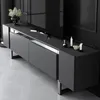 A modern TV stand with a sleek design, featuring a dark grey finish and silver accents. It is placed in a dimly lit room with a large television on top. Voir les images du produit