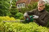 A man is trimming a hedge with an electric hedge trimmer in a garden. Produktbild-Vorschau