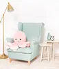 A pink plush octopus sits on a light blue armchair next to a gold floor lamp and small side tables with decorative items. Produktbild-Vorschau