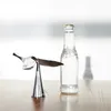 A chrome-finished bird-shaped bottle opener stands on a wooden table next to a clear glass bottle of water. Podgląd zdjęcia produktu