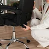 A person's hands are adjusting a lever on the back of a black office chair. Produktbild-Vorschau