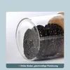 Close-up of black sesame seeds in a clear glass storage container with a wooden lid. Produktbild-Vorschau
