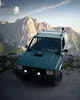 A green car parked on a rocky mountain road with a mountain range in the background. Anteprima dell’immagine prodotto